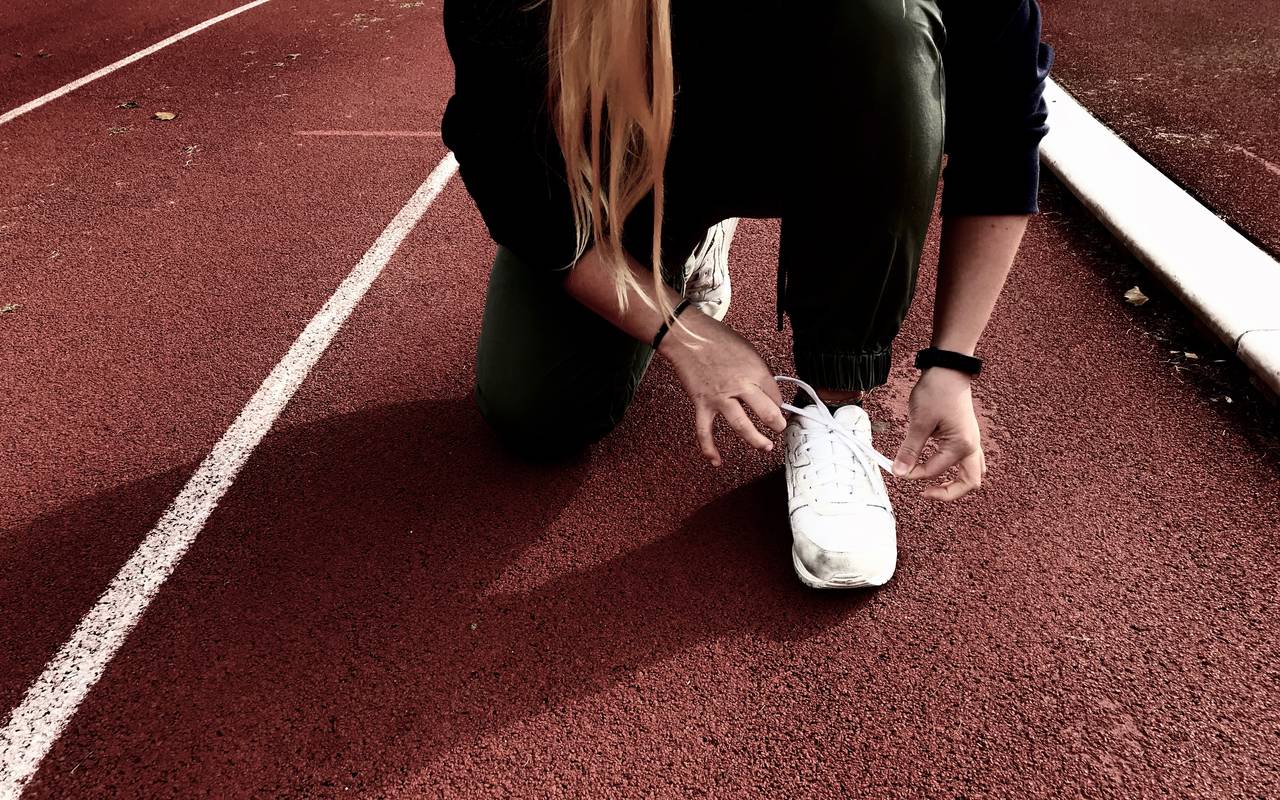 Sportler schnürt sich seinen weißen Turnschuh zum Laufen.