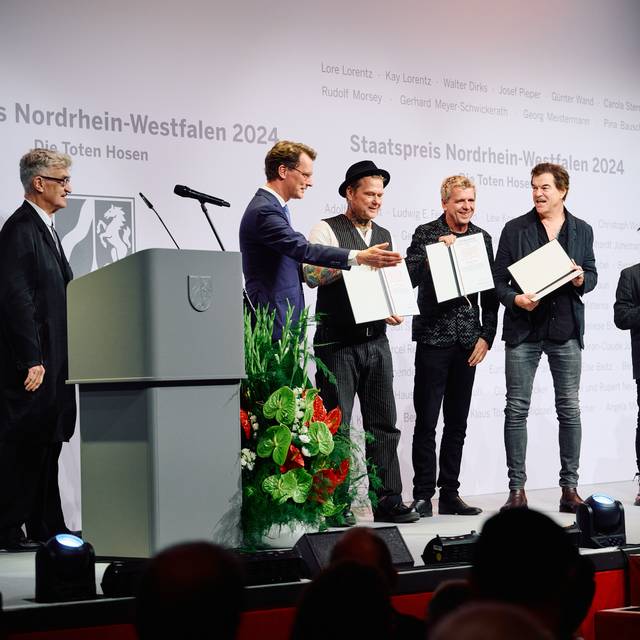 NRW-Ministerpräsident Hendrik Wüst verleiht den Toten Hosen den NRW-Staatspreis. Auch der Regisseur Wim Wenders ist auf der Bühne. Er hat die Laudatio gehalten.