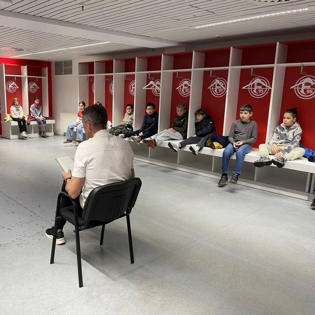 Fortuna-Legende Oliver Fink in der Heim-Kabine von Fortuna Düsseldorf. Er liest Kindern aus Niederkassel aus dem Buch "Woodwalkers" vor.
