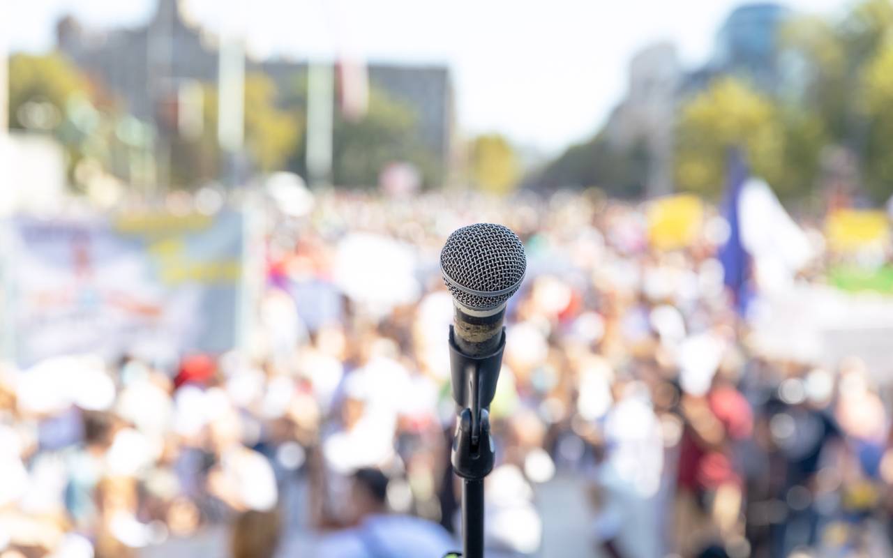 Ein Mikrofon vor einer Masse von Menschen. Die Menschen sind aber nur unscharf zu erkennen.