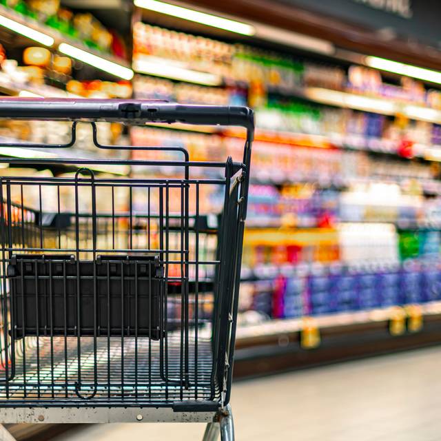 Ein leerer Einkaufswagen in einem Supermarkt. Im Hintergrund sind unscharf Regale zu erkennen.