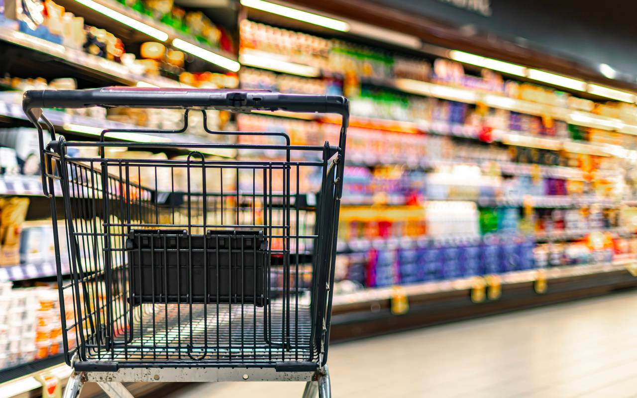 Ein leerer Einkaufswagen in einem Supermarkt. Im Hintergrund sind unscharf Regale zu erkennen.
