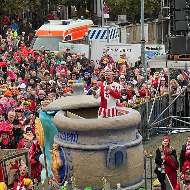 Der Hoppeditz hält seine Rede in einem Senftopf. Karnevalisten auf dem Marktplatz hören ihm zu.