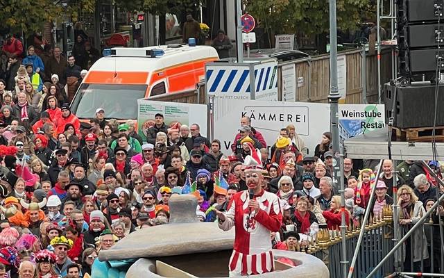 Der Hoppeditz hält seine Rede in einem Senftopf. Karnevalisten auf dem Marktplatz hören ihm zu.