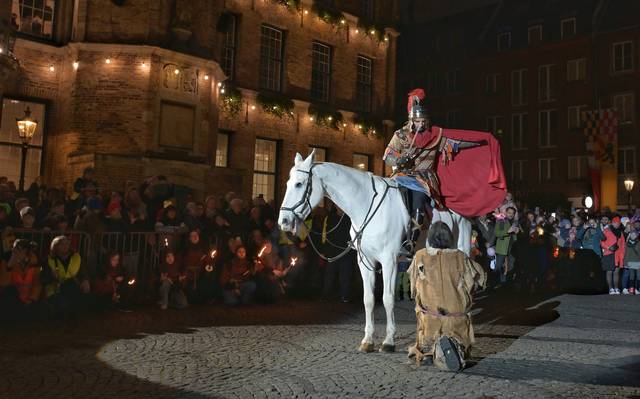 St. Martin teilt seinem Mantel mit einem armen Mann. Auf dem Martplatz wird das von vielen Menschen verfolgt.