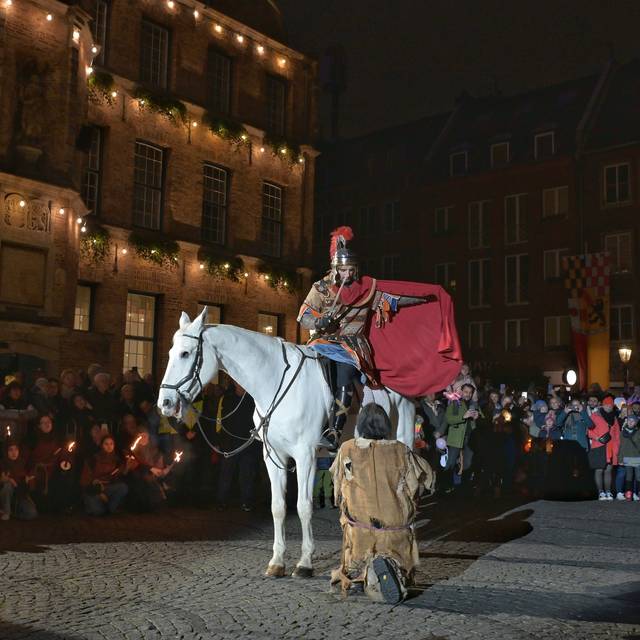 St. Martin teilt seinem Mantel mit einem armen Mann. Auf dem Martplatz wird das von vielen Menschen verfolgt.