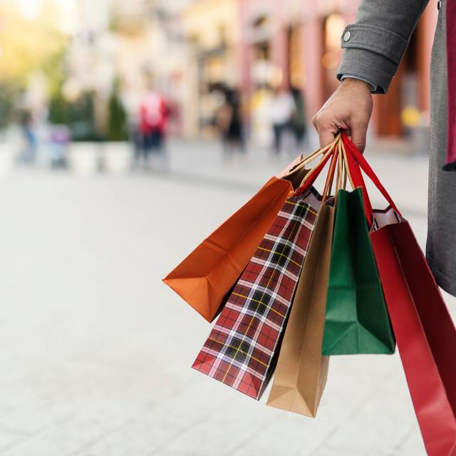 Verkaufsoffene Sonntage laden zum Shoppen ein. Ein unbekannter Mann hält vier unterschiedlich große Einkaufstüten in der Hand.
