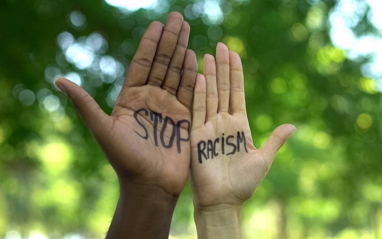 Zwei Hände werden in die Höhe gestreckt. Auf der linken Hand steht "Stop" und auf der rechten Hand "Racism".