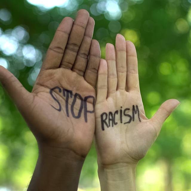 Zwei Hände werden in die Höhe gestreckt. Auf der linken Hand steht "Stop" und auf der rechten Hand "Racism".