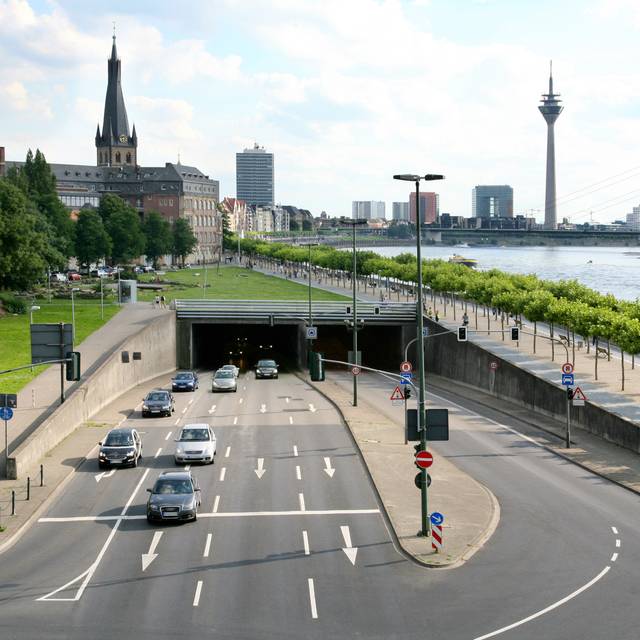 Der Rheinufertunnel und Autos. Hinter der Ausfahrt in Richtung Norden ist St. Lambertus, der Rheinturm und der Rhein erkennbar.