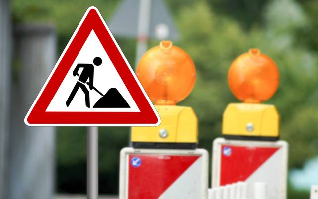 Ein Baustellenschild weist auf eine Baustelle hin. Im Hintergrund stehen zwei Warnbaken.
