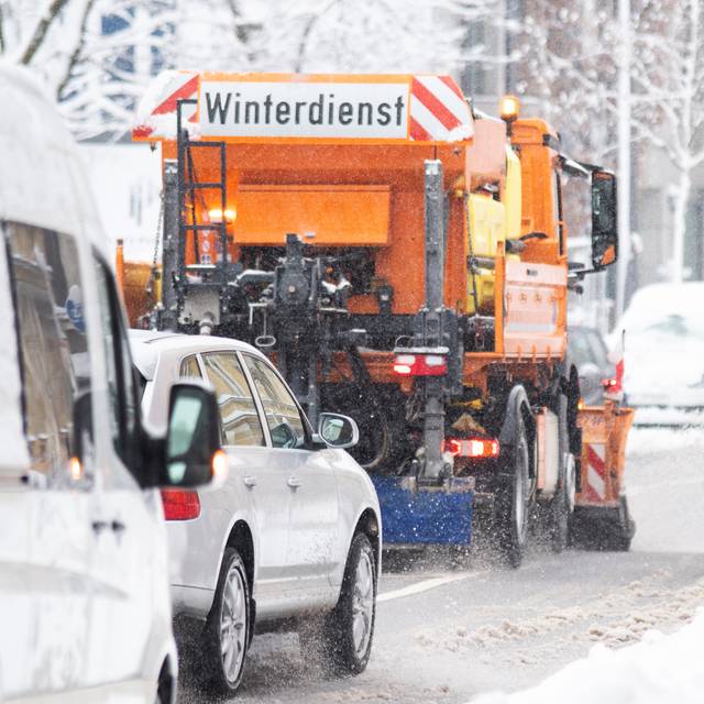 Ein Winterdienst-Fahrzeug im Einsatz. Hinter dem Streufahrtzeug fahren langsam weitere Autos.