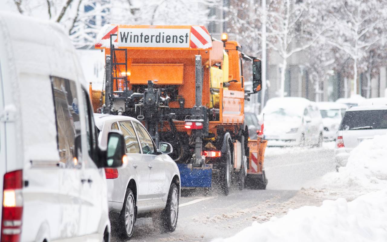 Ein Winterdienst-Fahrzeug im Einsatz. Hinter dem Streufahrtzeug fahren langsam weitere Autos.