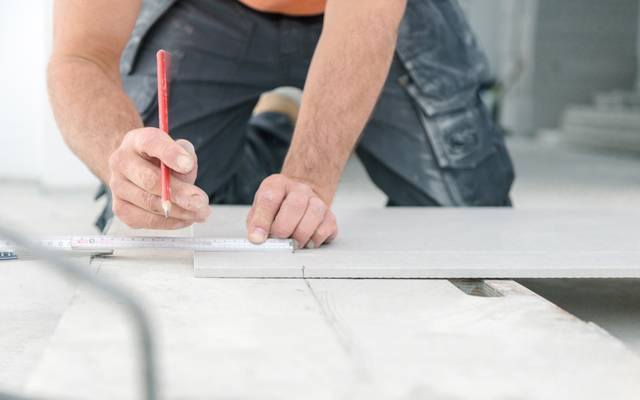 Ein Handwerker nimmt auf einer Arbeitsfläche mit einem Zollstock Maß.