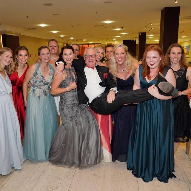 Der Krönungsball der Ges. RC Wilhelm Marx. Die Menschen tragen Abendgarderobe. Einige Frauen tragen den Major Jörg Münz auf Händen.