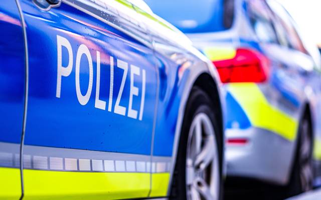 Ein Polizeiwagen auf einer Straße in Deutschland. Ein Polizeiwagen wird von der Seite abgebildet. Er ist blau-weiß mit gelben Streifen und in weißen Großbuchstaben steht "Polizei".