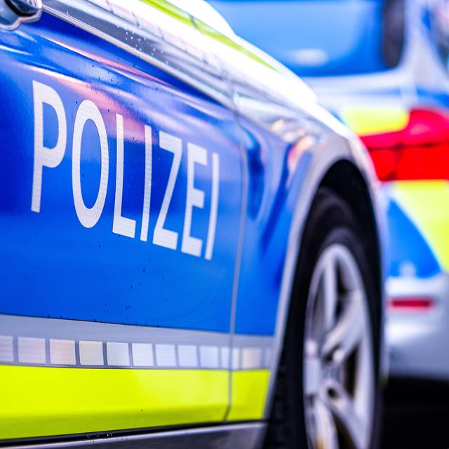 Ein Polizeiwagen auf einer Straße in Deutschland. Ein Polizeiwagen wird von der Seite abgebildet. Er ist blau-weiß mit gelben Streifen und in weißen Großbuchstaben steht "Polizei".