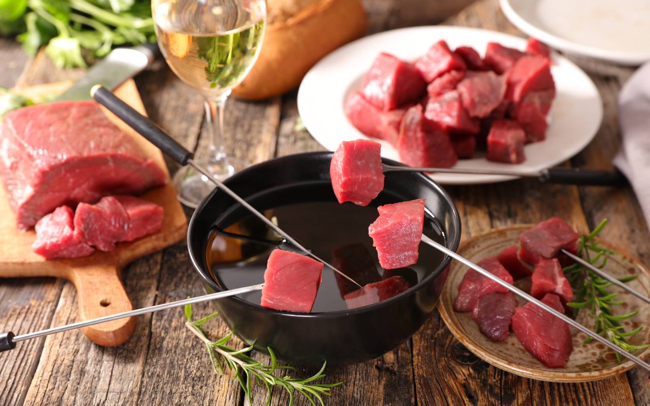 Ein Fondue-Topf mit Fleisch und einem Glas Weiswein.