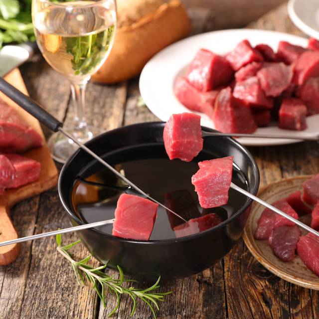 Ein Fondue-Topf mit Fleisch und einem Glas Weiswein.