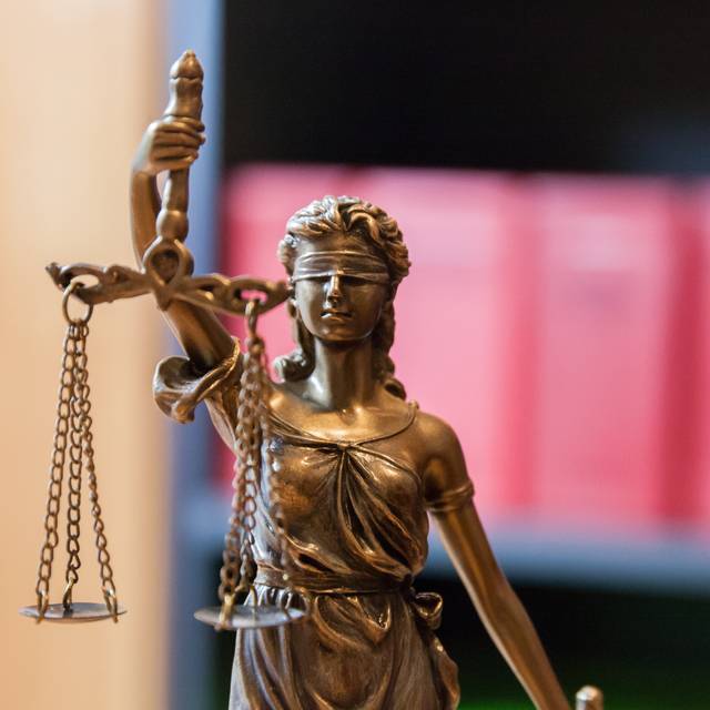 Justitia vor einem Bücherregal mit Gesetzbüchern.