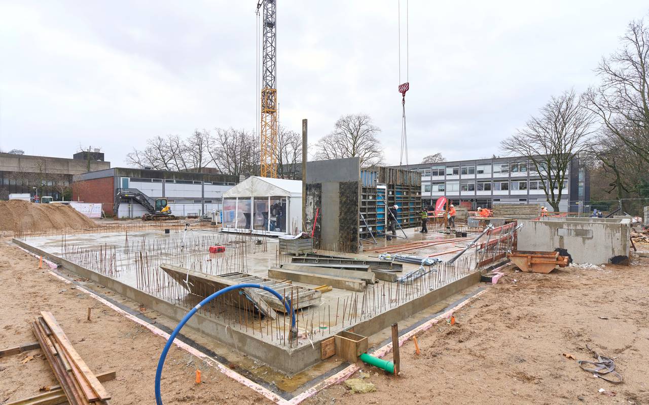 Baustelle für die Erweiterung der Rolandschule. Rund um den Grundstein befinden sich eine große Betonplatte, Kräne, Rohre und Kabel.