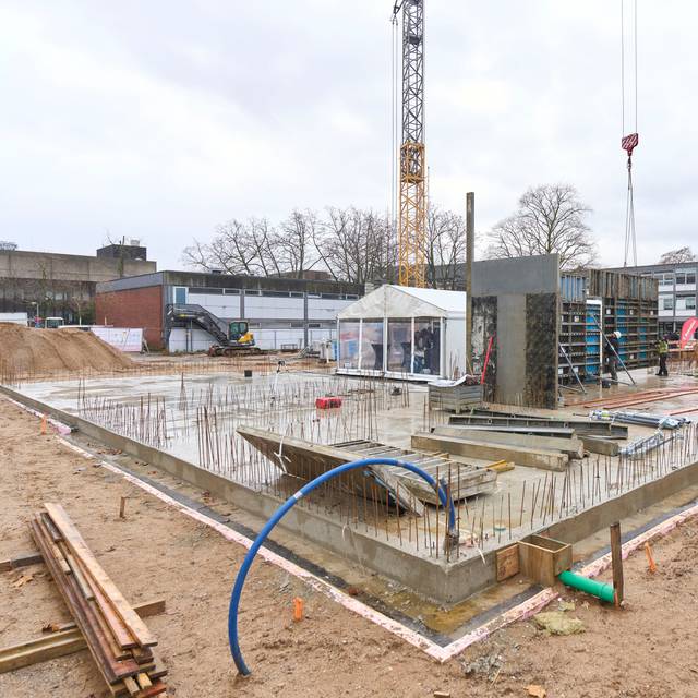 Baustelle für die Erweiterung der Rolandschule. Rund um den Grundstein befinden sich eine große Betonplatte, Kräne, Rohre und Kabel.