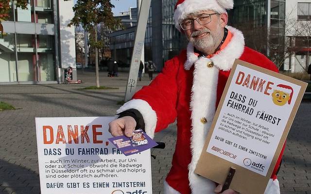 Ein verkleideter Nikolaus hält der Kamera einen Flyer und eine Zimtschnecke entgegen. In seiner Hand hält er ein Schild mit dem Slogan "Danke, dass du Fahrrad fährst!".