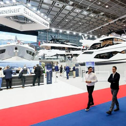 Messe boot: Drei Männer laufen im Vordergrund auf einem blau-roten Teppich durch die Messehalle. Sie unterhalten sich. Im Hintergrund kann man große Yachten und weiteres Publikum erkennen.