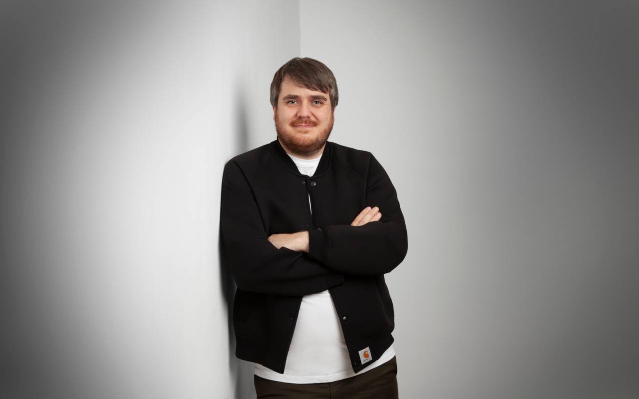 Der neue Gastro-Beauftragte der Stadt DüsseldorfJörn Topel posiert vor einer weißen Wand. Er trägt eine schwarze Hemd-Jacke und ein weißes T-Shirt und hat die Arme verschränkt