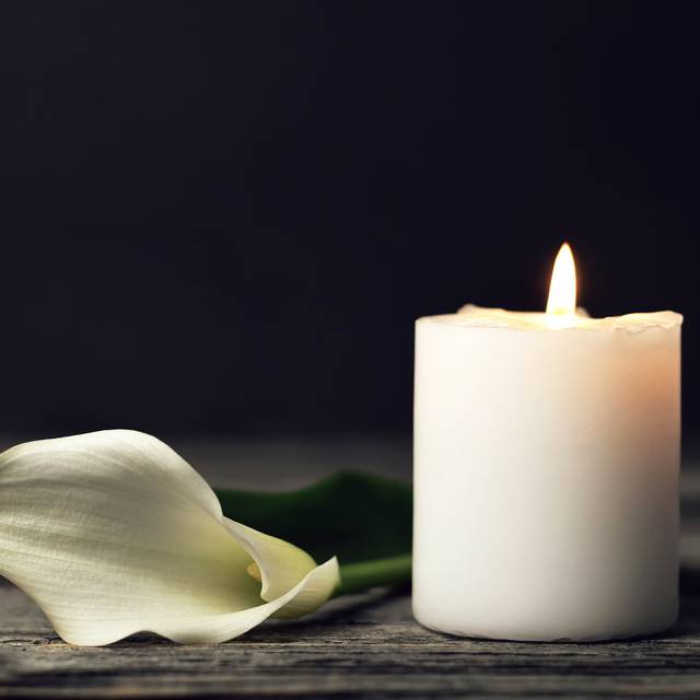 Brennende Kerze und weiße Calla-Lilie auf dunklem Hintergrund.