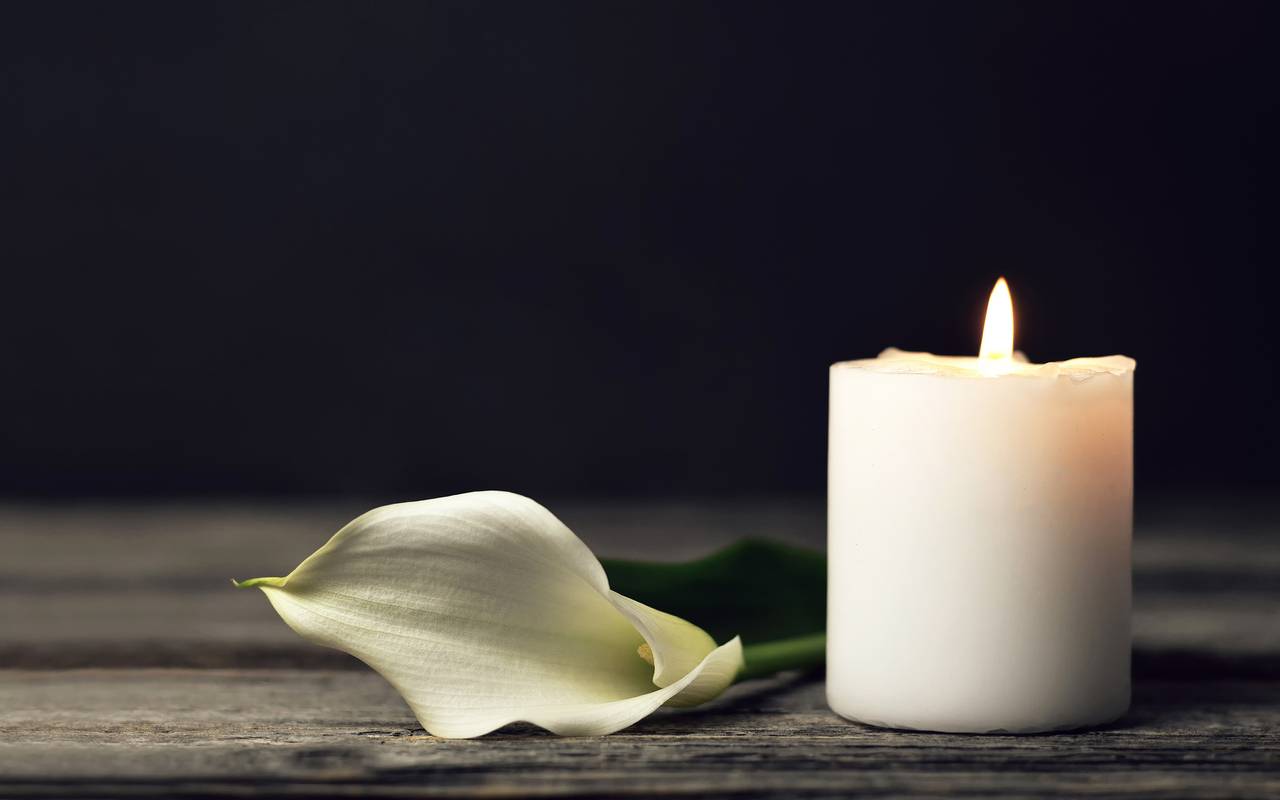 Brennende Kerze und weiße Calla-Lilie auf dunklem Hintergrund.