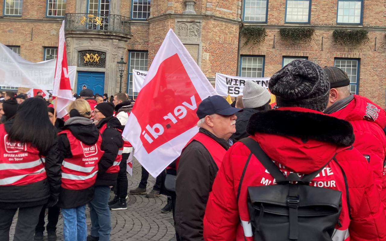Streikende Menschen vor dem Düsseldorfer Rathaus. Sie tragen Fahnen und rote Warnwesten.