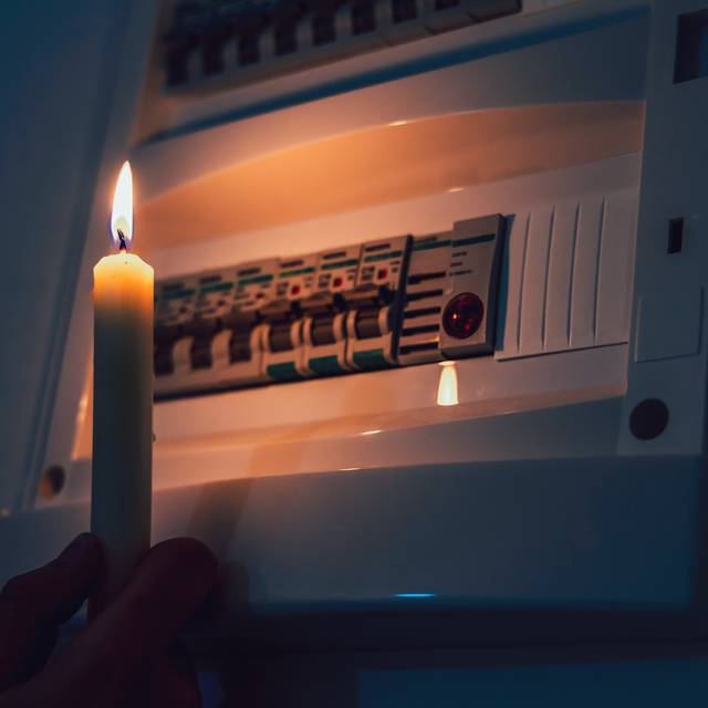 Ein Sicherungskasten während eines Stromausfalls. Der Kasten wird von einer brennenden Kerze beleuchtet.