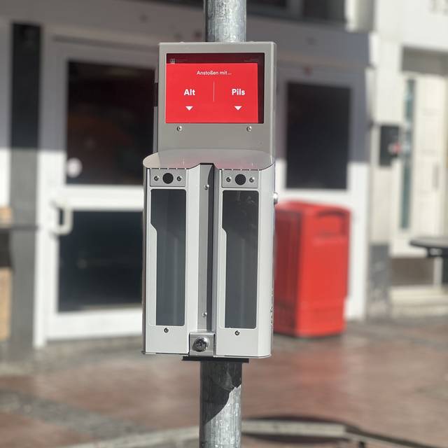 An einem Pfahl in der Altstadt hängen nebeneinander zwei Aschenbecher. Über einem steht auf einem roten Schild "Pils", über dem anderen "Alt".