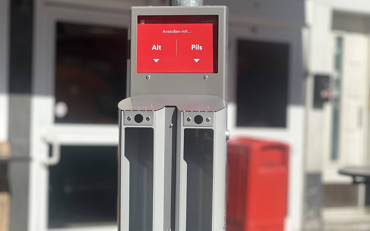 An einem Pfahl in der Altstadt hängen nebeneinander zwei Aschenbecher. Über einem steht auf einem roten Schild "Pils", über dem anderen "Alt".