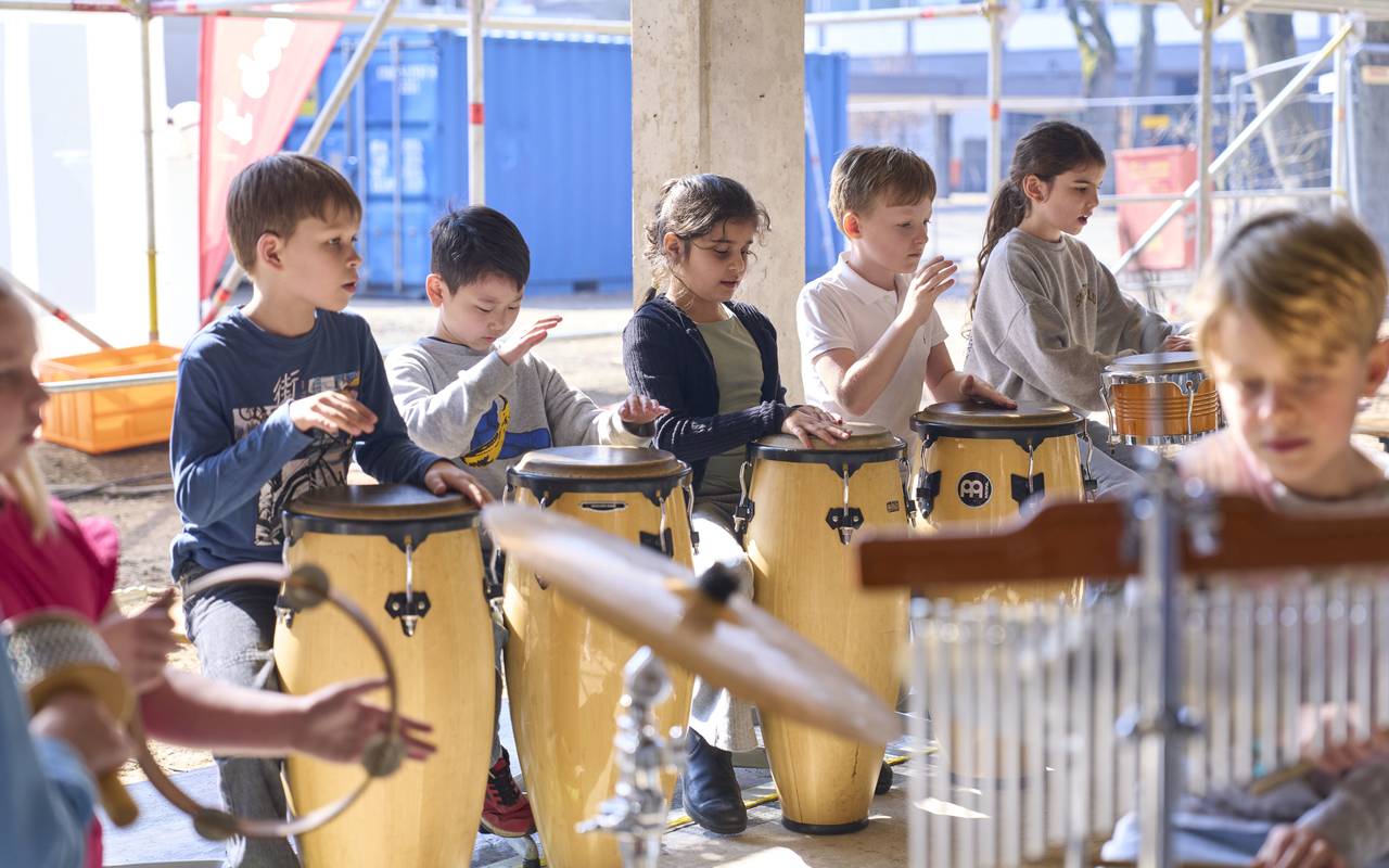 Schülerinnen und Schüler der Rolandschule mit Trommeln und anderen Musikinstrumenten. Die Kinder spielen zum Richtfest für den Erweiterungsbau. Im Hintergründ sind Baugerüste zu sehen.