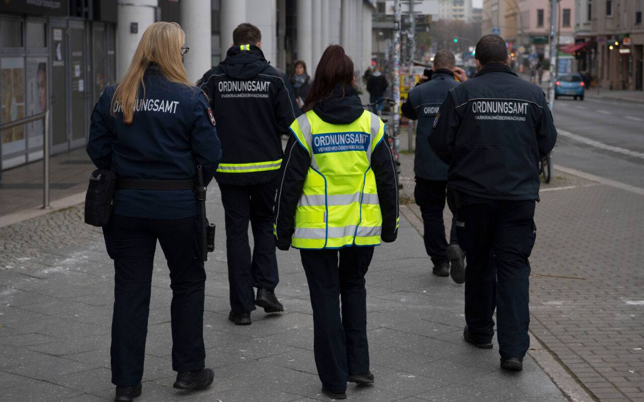 Städtische Mitarbeiter werden von Sicherheitskräften zu einem Termin begleitet.