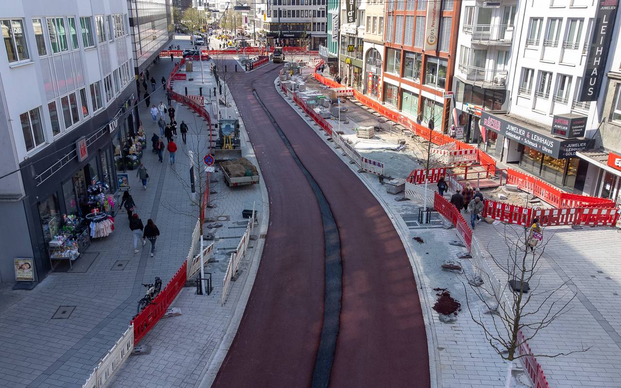 Zwei rot markierte Radspuren zwischen dem Wehrhahn und der Schadowstraße. Die unfertigen Radwege führen durch eine Baustelle, links und rechts sind Absperrungen zu sehen. Dahinter befinden sich Geschäftshäuser auf der linken und rechten Straßenseite.