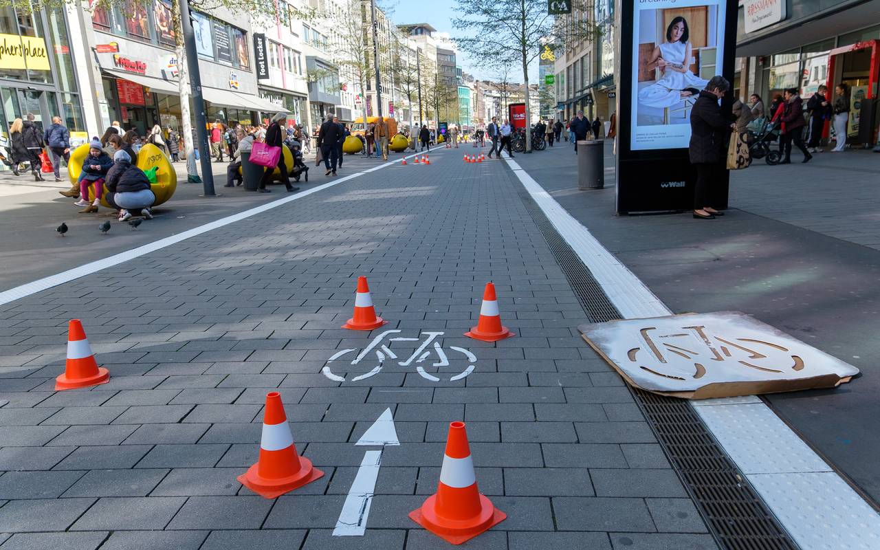 Der Radweg auf der Schadowstraße ist mit weißer Farbe teilweise neu markiert. Zu sehen ist unter anderem ein Fahrrad-Piktogramm. Links und rechts vor den Geschäftshäusern sind Menschen zu Fuß unterwegs.