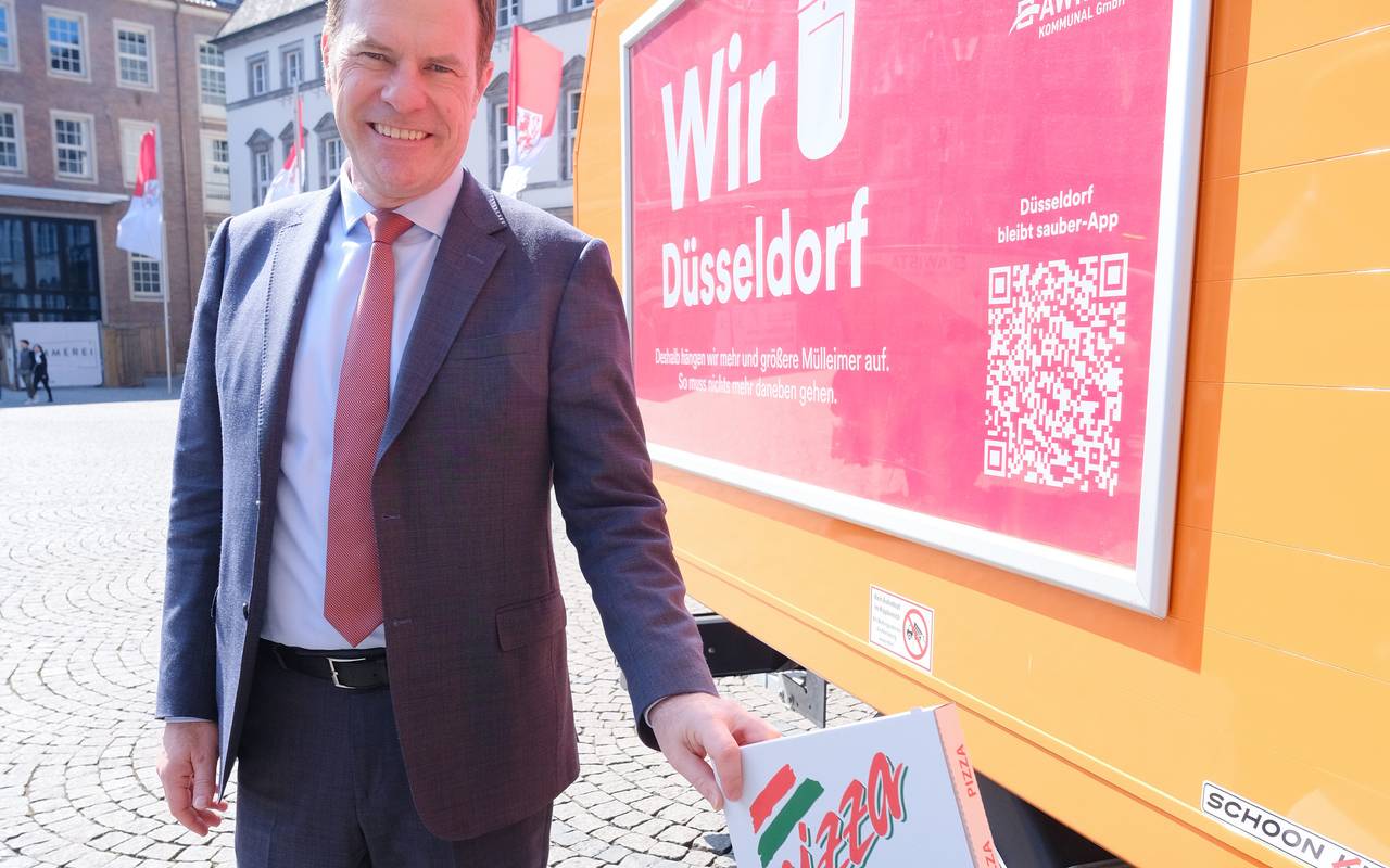 OB Keller wirft vor dem Rathaus einen Pizzakarton in einen Mülleimer mit extra breitem Schlitz. Daneben ist ein AWISTA-Fahrzeug zu sehen.