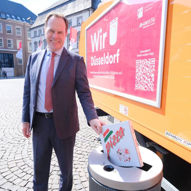 OB Keller wirft vor dem Rathaus einen Pizzakarton in einen Mülleimer mit extra breitem Schlitz. Daneben ist ein AWISTA-Fahrzeug zu sehen.