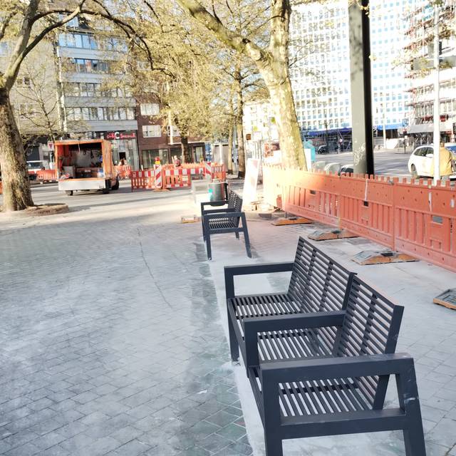 Neue, kleinere Bänke stehen auf dem Worringer Platz. Sie ersetzen die alten Glasbausteine. Im Hintergrund sind Baufahrzeuge zu sehen. Es laufen noch weitere Asphaltarbeiten.