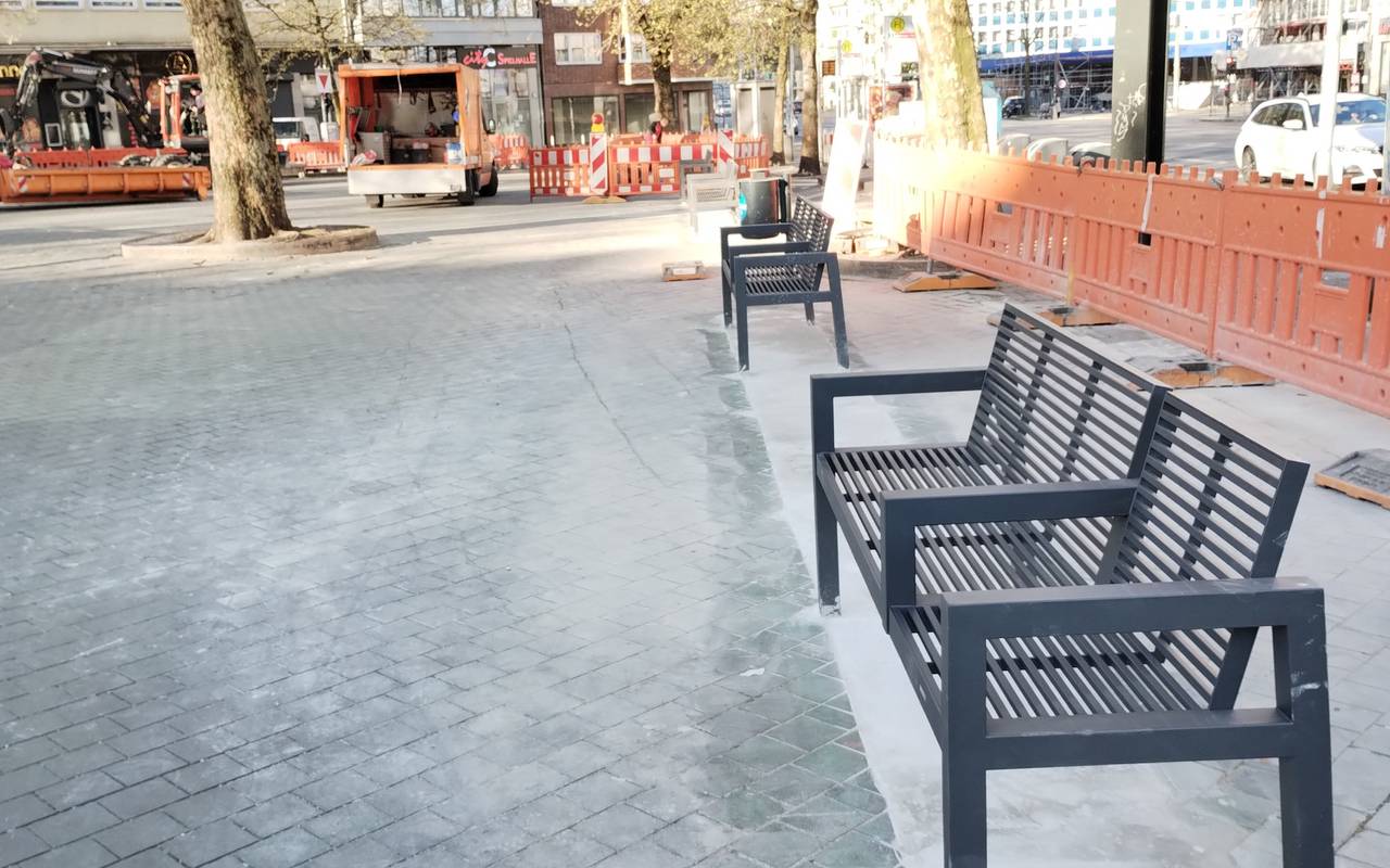 Neue, kleinere Bänke stehen auf dem Worringer Platz. Sie ersetzen die alten Glasbausteine. Im Hintergrund sind Baufahrzeuge zu sehen. Es laufen noch weitere Asphaltarbeiten.