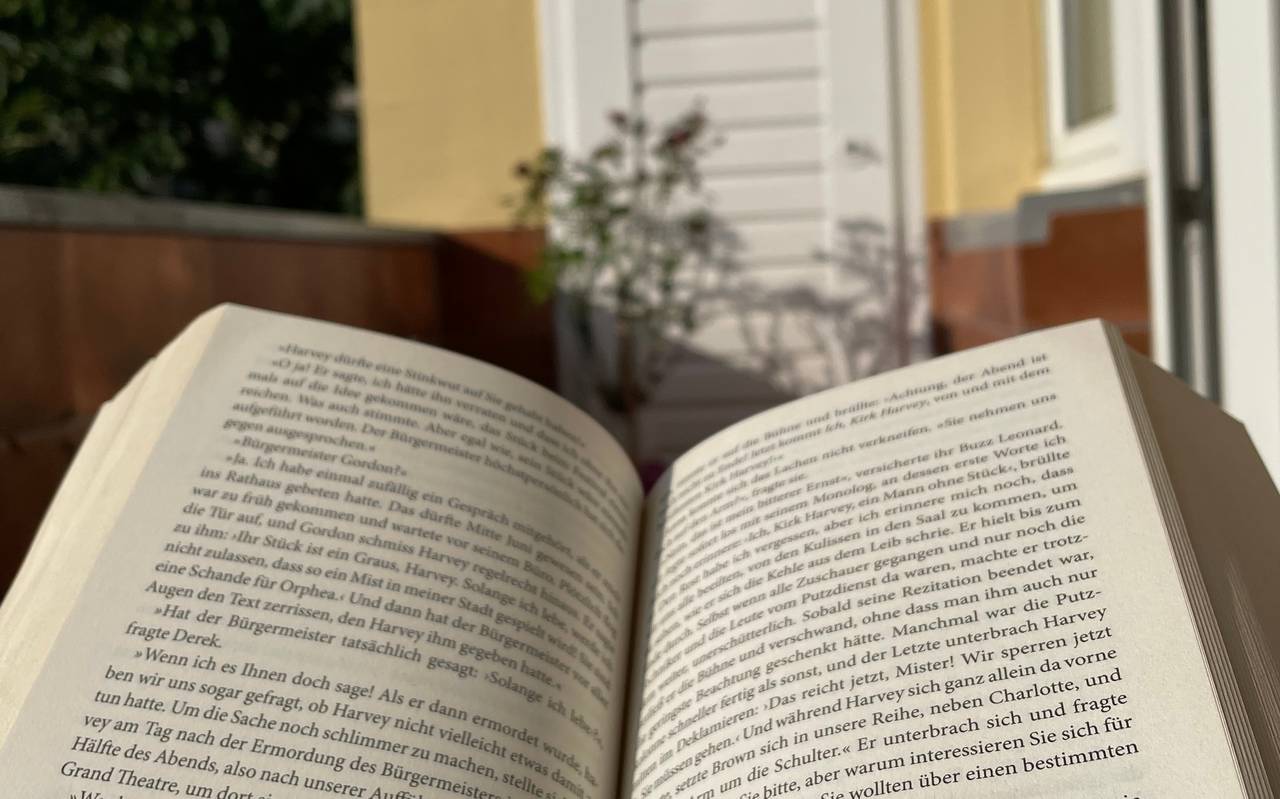 Ein aufgeschlagenes Buch. Im Hintergrund ist ein Balkon zusehen, mit einer weißen Tür und einer gelben Wand.