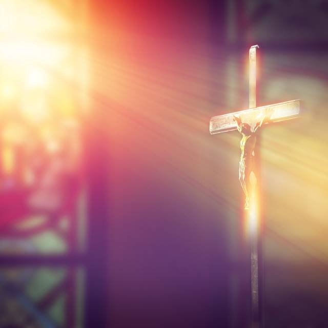Kruzifix, Jesus am Kreuz in der Kirche mit Lichtstrahlen von Buntglasfenstern.