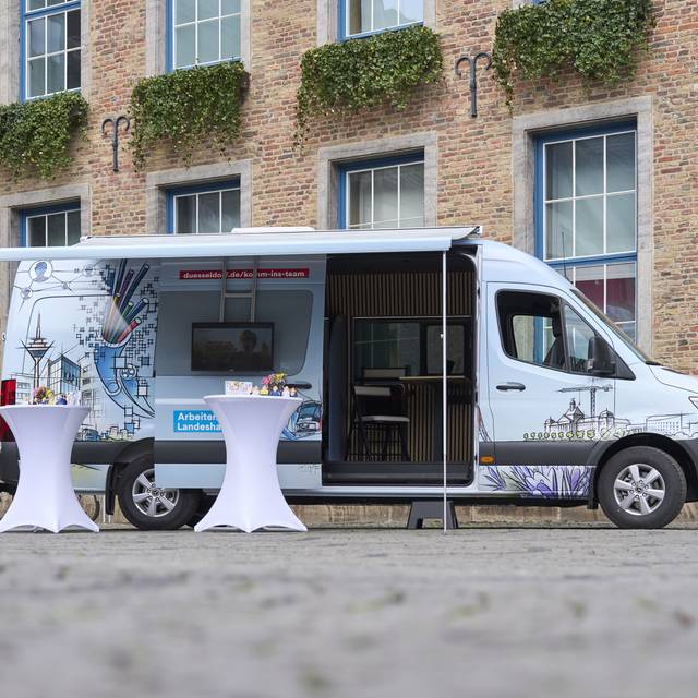 Der Karriere-Bus der Stadt steht vor dem Düsseldorfer Rathaus. Die Seitentüre ist geöffnet. Menschen können sich hier für einen Job bewerben.