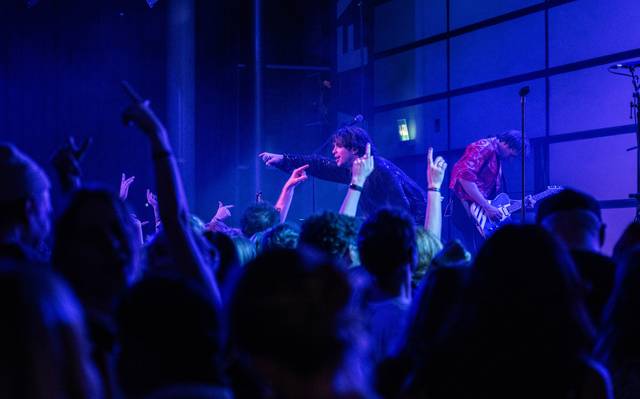 Feiernde Menschen vor einer Festival Bühne. Auf der Bühne ist der Künstler Bibiza, er streckt sein Mikrofon in die Menge.