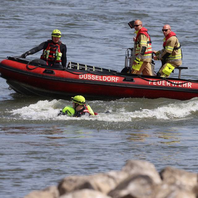 Feuerwehrboot mit Besatzung bei einer Übung auf dem Rhein. Im Wasser sind dabei ein Retter und eine zu rettende Person.