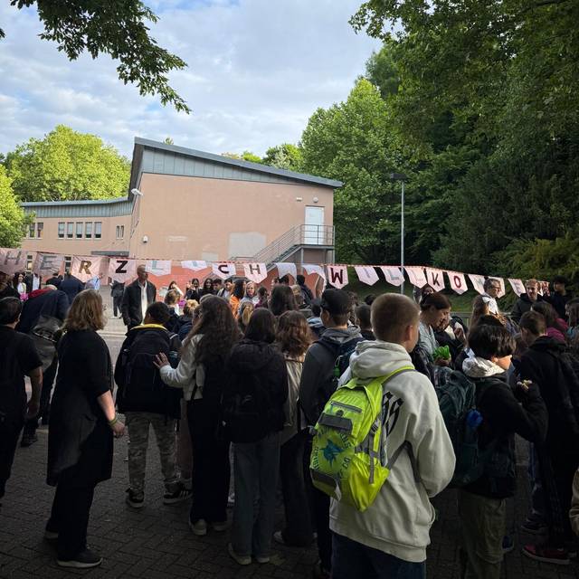 Die Schülerinnen und Schüler aus Erkrath laufen durch das Schultor, darüber hängt der Schriftzug Herzlichen Willkommen.