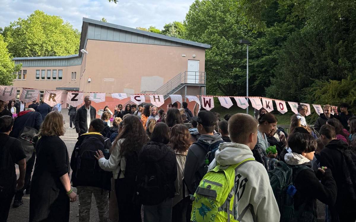 Die Schülerinnen und Schüler aus Erkrath laufen durch das Schultor, darüber hängt der Schriftzug Herzlichen Willkommen.